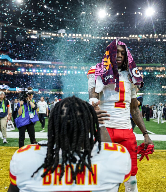Two football players in red and white uniforms celebrate on a field with confetti falling. One player stands with a towel on his head, extending his hand, while the other faces him with "BROWN" visible on his jersey. Spectators and media are in the background.