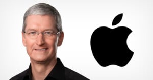 A man with short gray hair and glasses, wearing a black shirt, is smiling in front of a large black Apple logo on a white background.