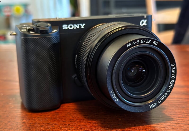 A Sony Alpha digital camera with a zoom lens rests on a wooden surface, showing the lens markings and camera details clearly.