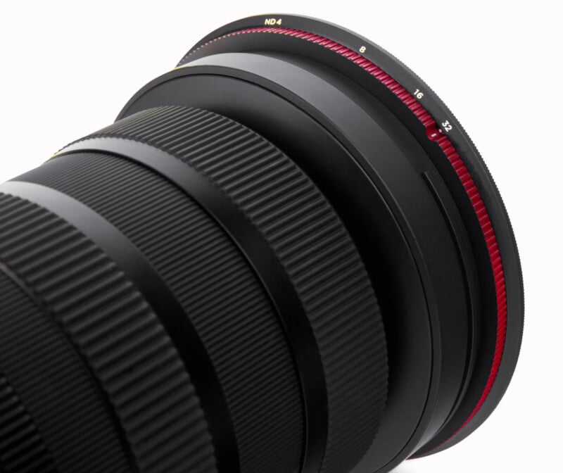 Close-up of a black camera lens with textured rubber grip rings and a red-rimmed ND filter attached, showing detailed markings and adjustment numbers on the filter.