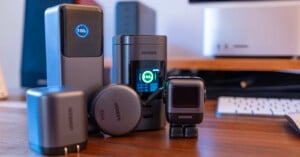 Several UGREEN electronic devices, including chargers and adapters, are displayed on a wooden desk in front of a computer setup, with digital screens showing charging icons.