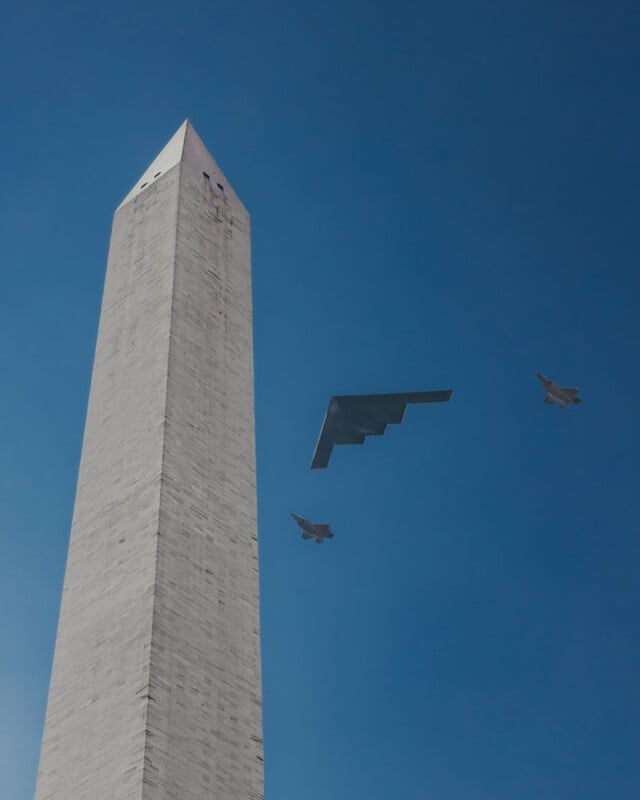 The Washington Monument is seen against a clear blue sky, with a stealth bomber and two fighter jets flying nearby.