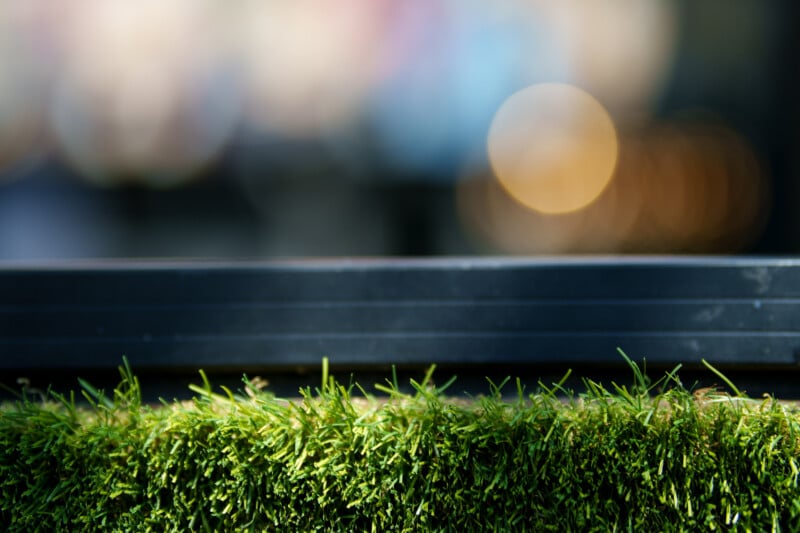 Close-up of green grass with a blurred black horizontal bar above it and a soft, out-of-focus background featuring colorful circular light bokeh.