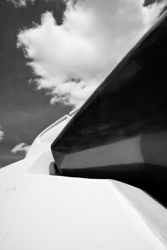 A close-up, upward view of a modern white and black architectural structure set against a partly cloudy sky, photographed in black and white.