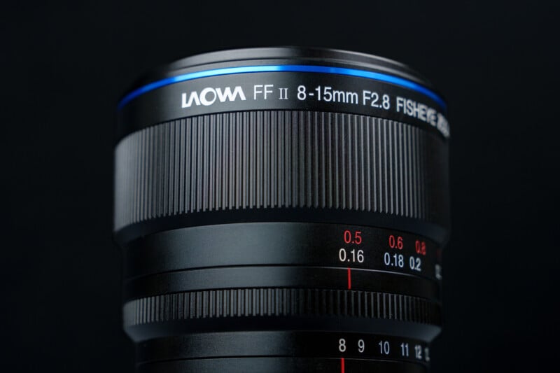Close-up of a Laowa FF II 8-15mm F2.8 fisheye camera lens against a black background, showing the lens markings and blue accent ring near the top.