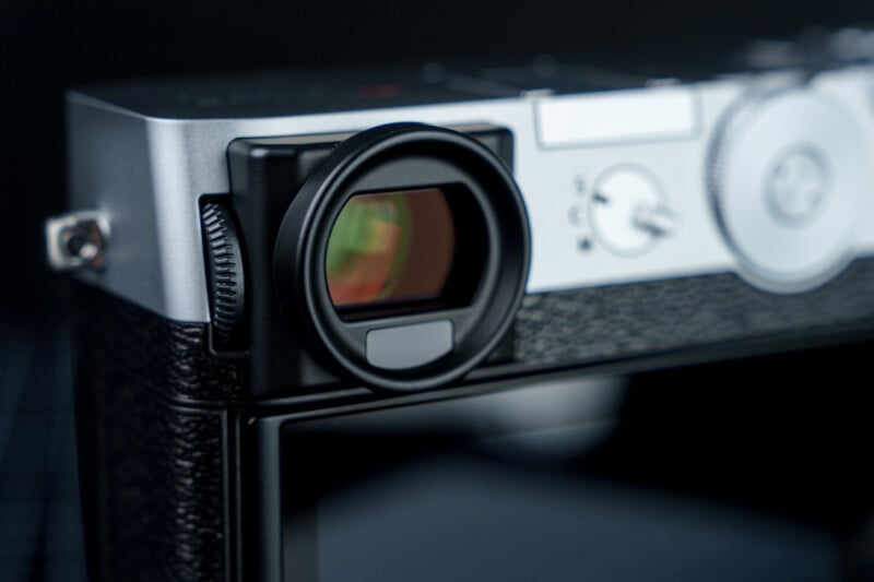 Close-up of a vintage-style camera showcasing the viewfinder and adjustment dials. The camera has a metallic finish with textured black accents and a small knob on the side. The background is dark, emphasizing the camera's retro design.