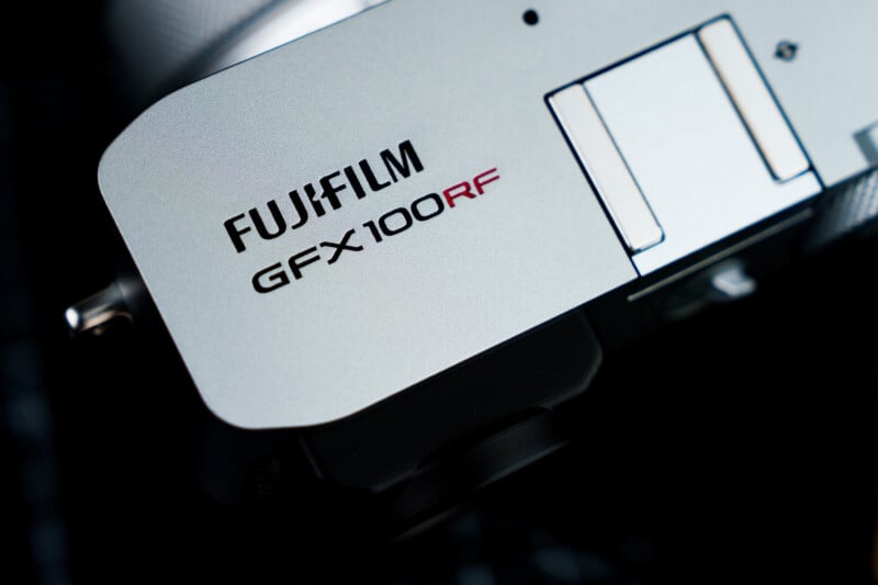Close-up of a Fujifilm GFX100RF camera body, showcasing its sleek, metallic finish and the model name printed prominently in black and red lettering on the top surface.