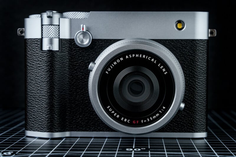A vintage-style camera with a Fujinon Aspherical Lens, featuring a textured black body and silver accents, is placed on a gridded surface marked with angles and measurements.