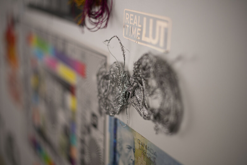 Close-up of a wall with colorful artwork, a silver tangled string, a Canadian bill, and a label reading “REAL TIME LUT” in focus, with the background softly blurred.
