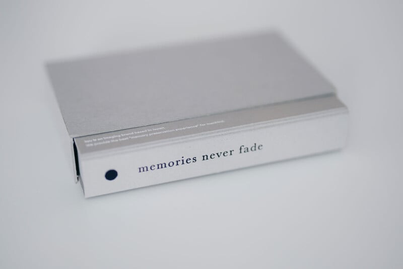 A closed, gray hardcover book lying on a white surface. The spine displays the phrase "memories never fade" in lowercase black letters. The book has a minimalist design.