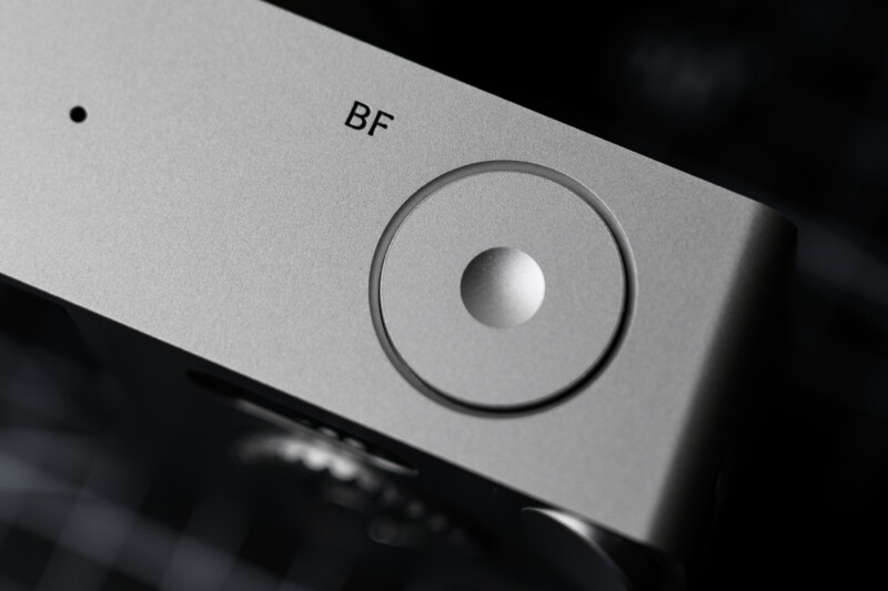 Close-up of a silver electronic device featuring the letters "BF" and a circular button on its surface. The background is out of focus, highlighting the sleek and minimalistic design of the device.