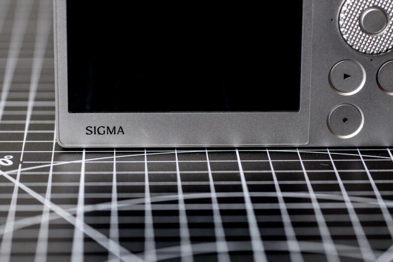 Close-up of a Sigma camera's rear display and buttons on a black grid pattern surface.