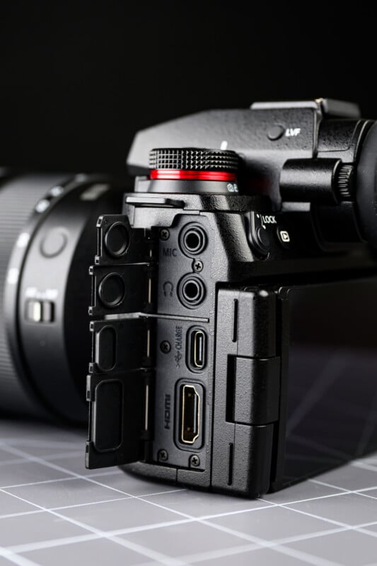 Close-up of a digital camera with its side panel open, revealing ports including HDMI, USB, a mic input, and headphone jack, against a dark, blurred background.