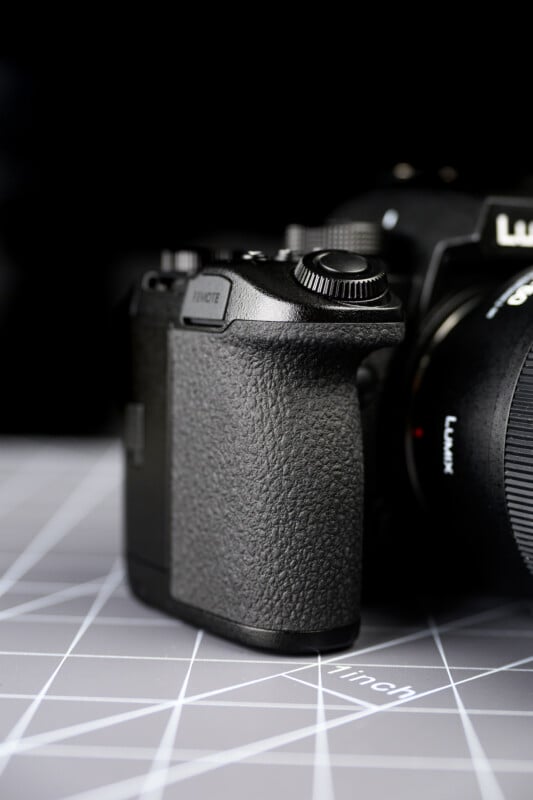 A close-up of a black digital camera placed on a geometric-patterned surface, showing the textured grip and part of the lens under bright lighting.