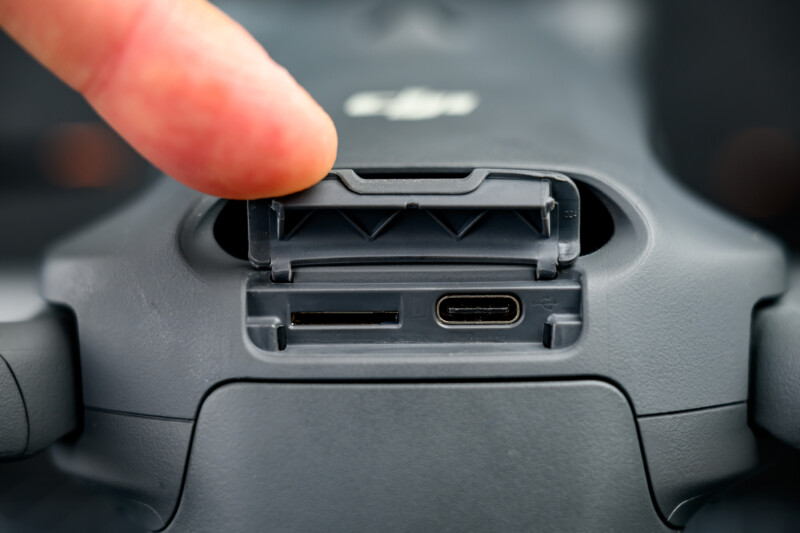 A close-up of a person’s finger opening a flap on a gray DJI device, revealing a microSD card slot and a USB-C port.