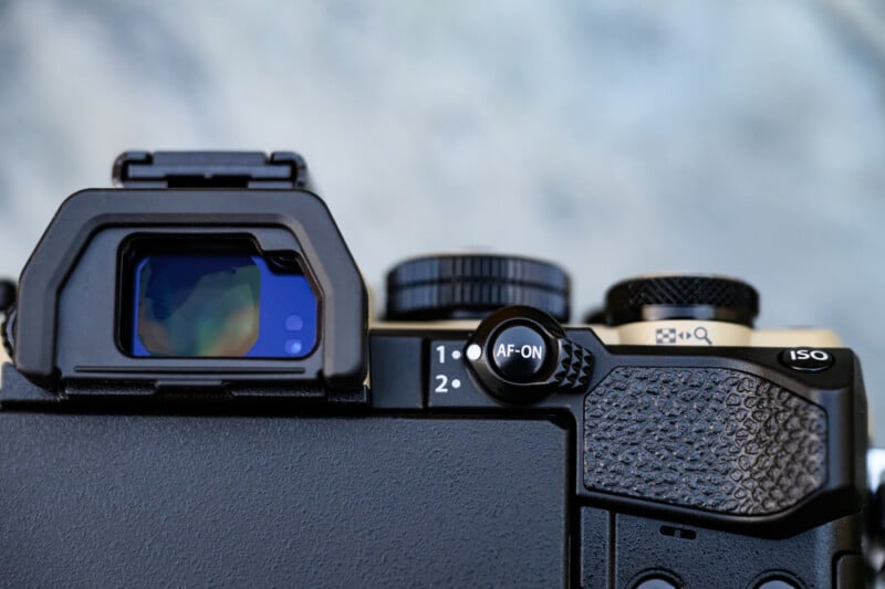 Close-up of a camera's electronic viewfinder, control dials, and buttons, including "AF-ON," "ISO," and customizable function buttons, with a textured grip on the right side. Background is out of focus.