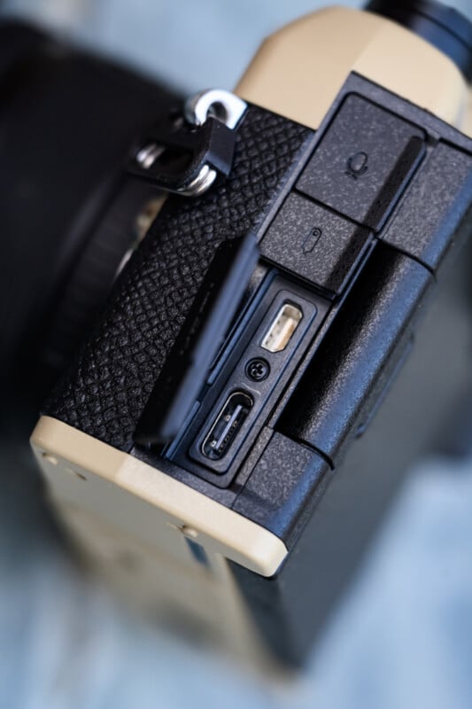 Close-up of a camera’s side panel, showing an open flap revealing a USB-C port and a mini HDMI port, with textured grip and part of the lens visible.