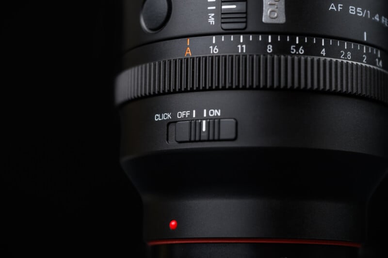 Close-up of a camera lens showing a "CLICK OFF ON" switch, a focus ring with distance markings, and a red alignment dot, all set against a black background.