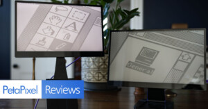 Two computer monitors displaying pixel art designs are placed on a wooden table, surrounded by greenery. The image is branded with "PetaPixel Reviews" in the bottom left corner, suggesting a tech or gadget review setting.