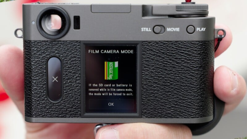 A close-up of the back of a digital camera shows a screen displaying a message about film camera mode, warning that removing the SD card or battery will force the mode to exit. A hand is holding the camera.