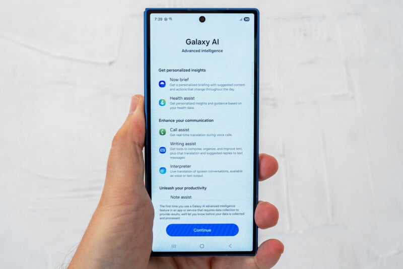 A hand holding a smartphone displaying a “Galaxy AI” setup screen with options for AI features like news brief, health assist, call assist, writing assist, interpreter, and note assist.