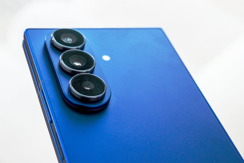 Close-up of the back of a blue smartphone featuring three large camera lenses arranged vertically in the top left corner.