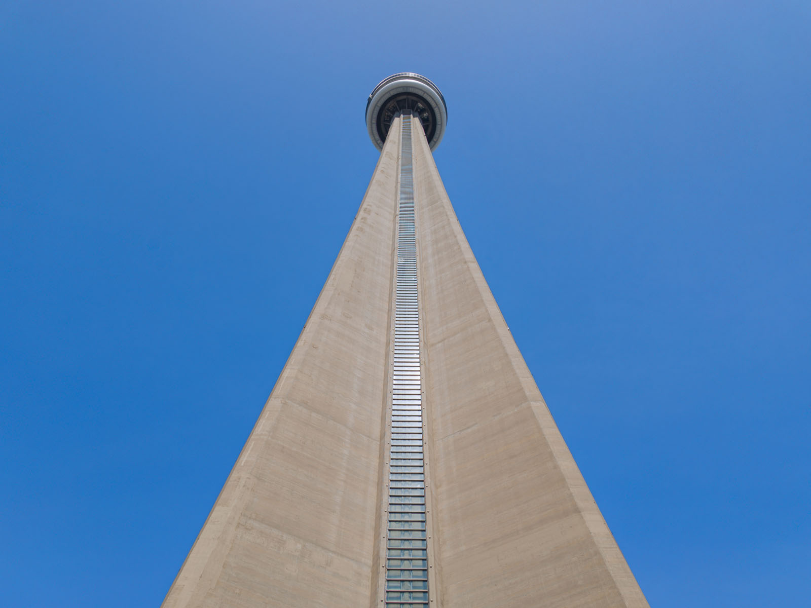 View from the base of a tall concrete observation tower, looking straight up against a clear blue sky. The perspective emphasizes the height and triangular shape of the structure.