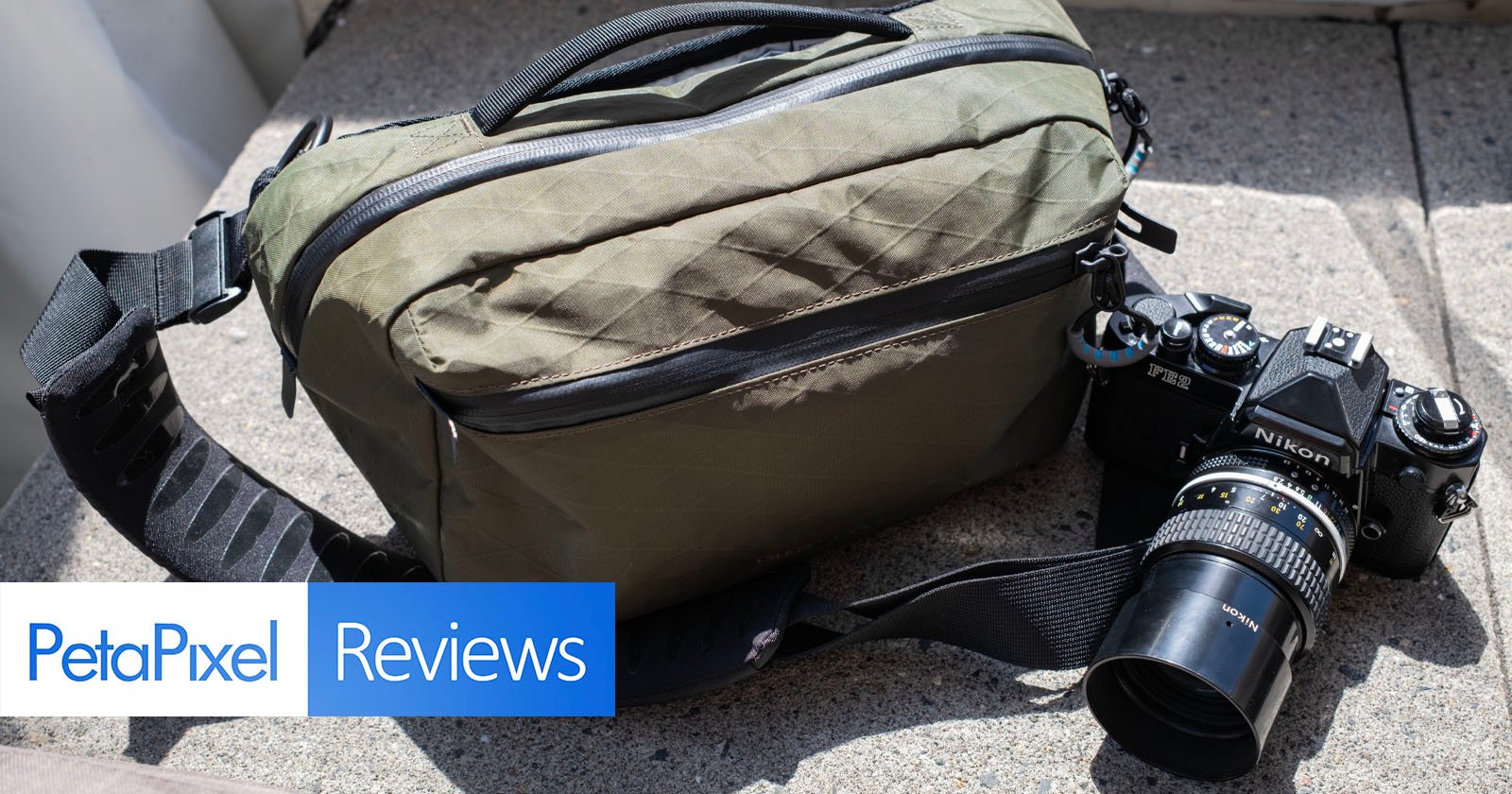 A green camera bag and a vintage Nikon film camera with a lens rest on a concrete surface. The lower left corner displays the "PetaPixel Reviews" logo.