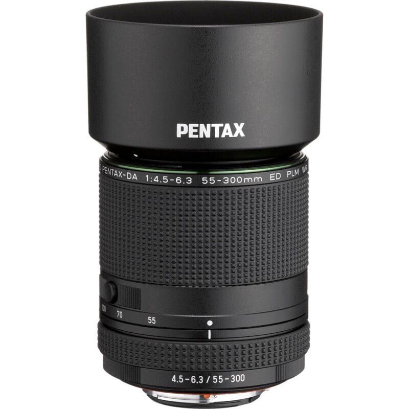 A Pentax camera lens with a lens hood attached, labeled "PENTAX" on the front. The zoom range of 55-300mm and aperture values are visible on the barrel. The lens is black with textured grip rings.