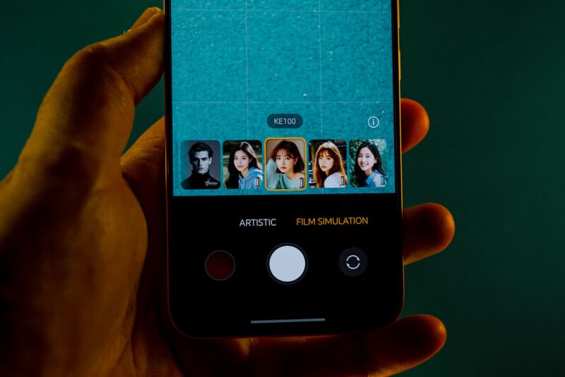 A hand holds a smartphone displaying a camera app with a grid overlay and several filter options, including portraits, under the “Film Simulation” setting. The screen features a large white shutter button at the bottom.