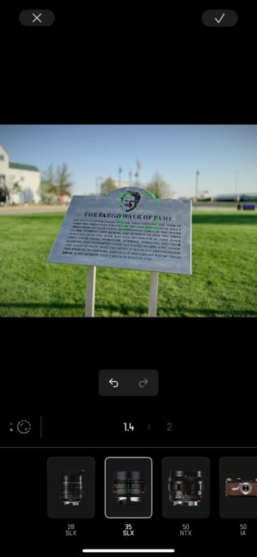 A metal plaque titled "The Fargo Walk of Fame" stands on a lawn, with a blurred building and trees in the background. The plaque features text and a man's portrait at the top.