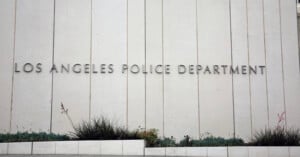 Large, modern concrete building facade with "Los Angeles Police Department" in metal letters; low landscaping with various small plants in front.
