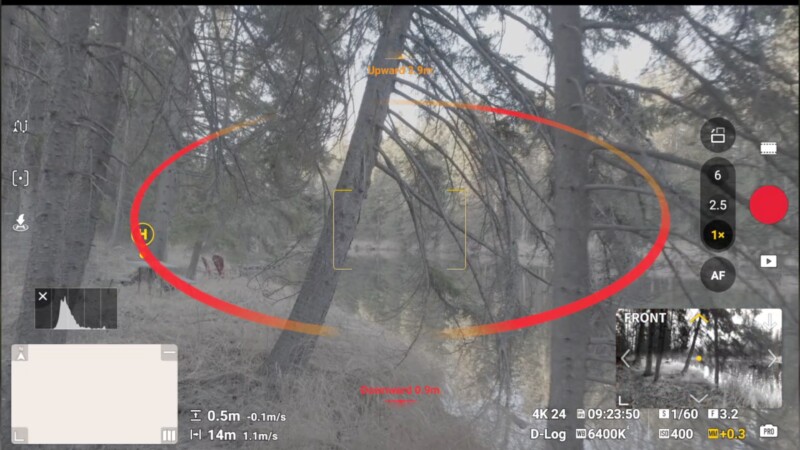 A drone camera interface shows a forest scene with tall trees. Onscreen controls and data are visible, along with a red oval overlay highlighting a specific area. Two small figures can be seen in the background among the trees.