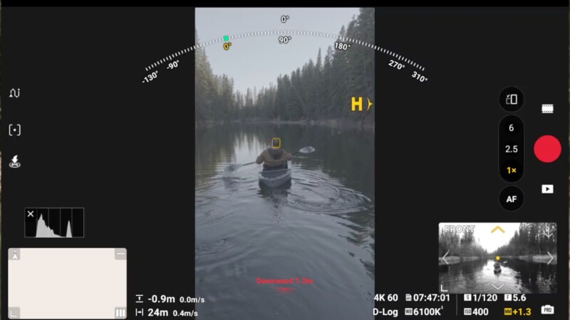 A person paddles a canoe on a calm lake surrounded by pine trees. The image is framed by drone camera controls and telemetry data, with focus indicators and recording settings visible on the screen.