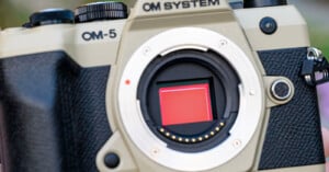 Close-up of an OM SYSTEM OM-5 digital camera with the lens removed, revealing the image sensor inside the camera body.