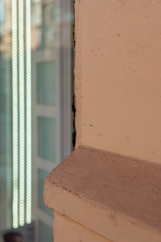 A close-up of a beige corner of a building with a blurred glass window in the background, featuring vertical lines of bright white lights.
