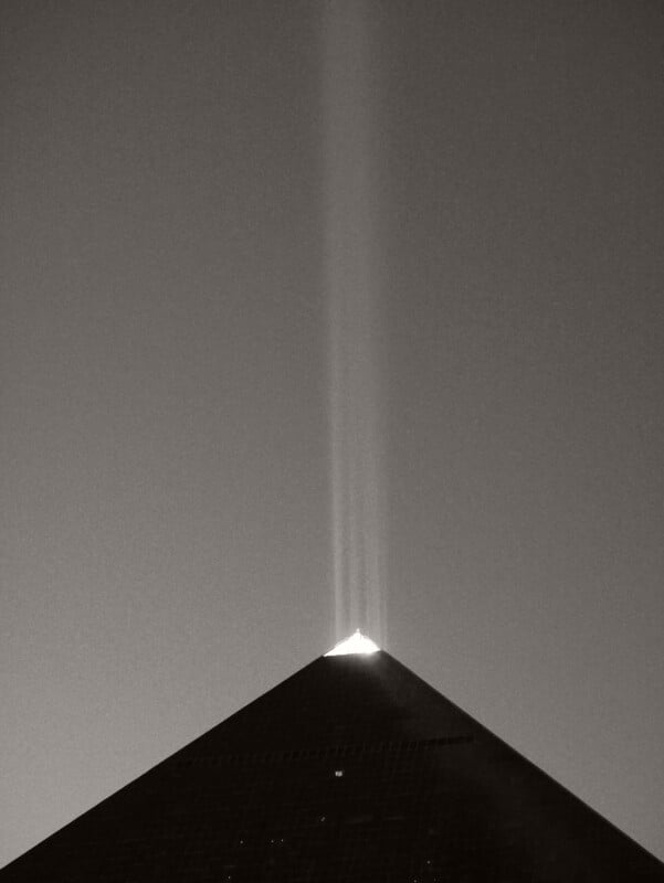 A pyramid-shaped building at night with bright beams of light shining straight up from its apex into the dark sky.