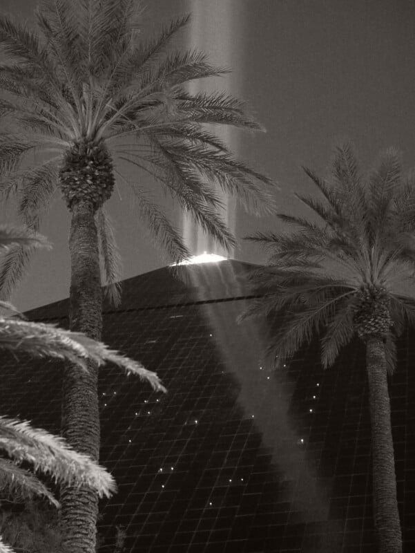 Black-and-white photo of the Luxor Hotel pyramid in Las Vegas at night, with palm trees in the foreground and a bright beam of light shining upward from the pyramid’s apex.