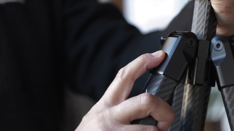 A close-up of a person's hand pressing a button on a sleek, black, carbon fiber device, possibly a handle or tool, with a blurred background.
