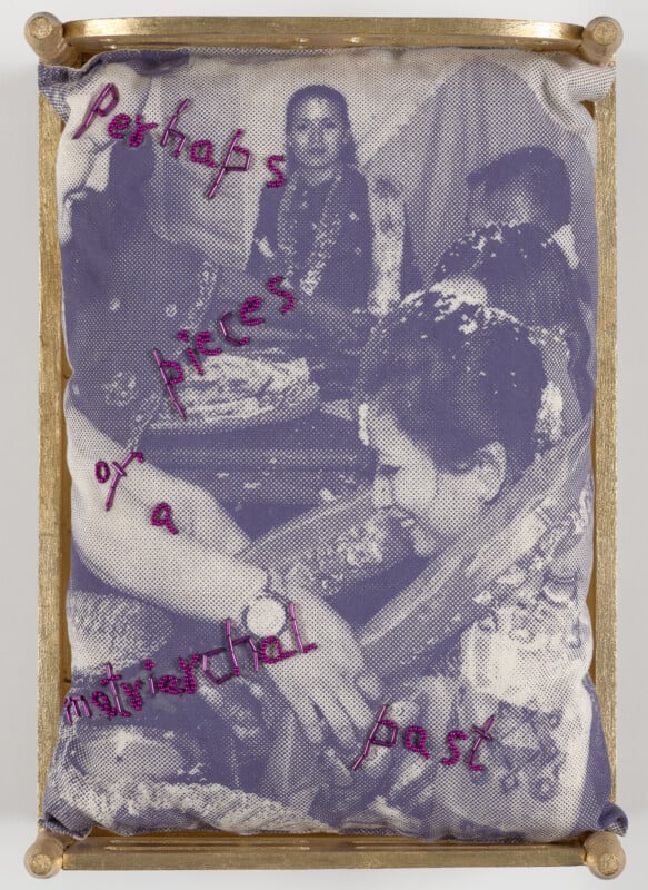 A fabric artwork with a black-and-white photo of people interacting, overlaid with pink embroidered text reading: "Perhaps on pieces of a matriarchal past," framed by a gold border.