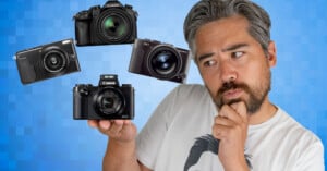 A man with gray hair and a beard looks thoughtfully at four floating cameras against a blue checkered background, holding one camera in his hand.