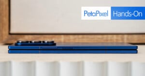 A blue foldable smartphone shown closed and viewed from the side, with camera lenses visible. The image features "PetaPixel Hands-On" text in the upper right corner.