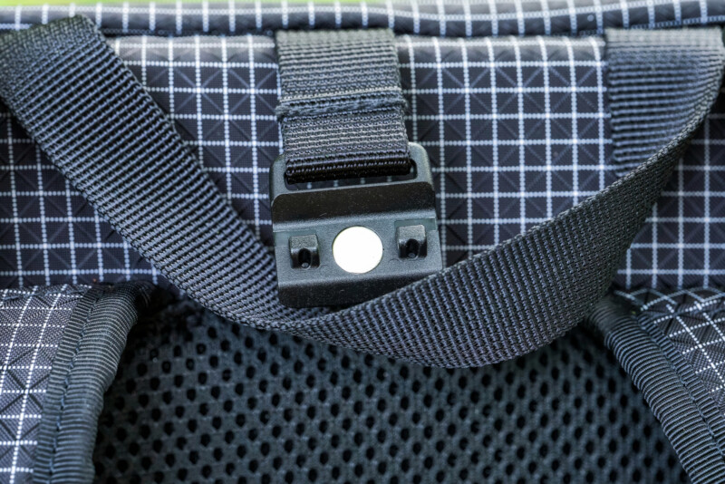 Close-up of a black strap with a plastic buckle on a backpack featuring a white grid pattern and breathable mesh padding.