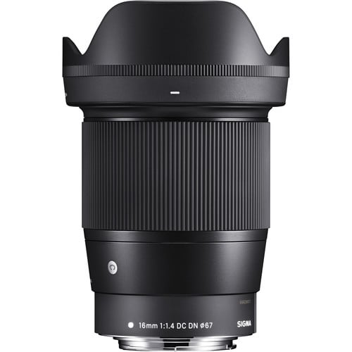 A Sigma 16mm f/1.4 DC DN camera lens with a wide lens hood, black body, ribbed focus ring, and white text indicating its focal length, aperture, and filter size, set against a white background.