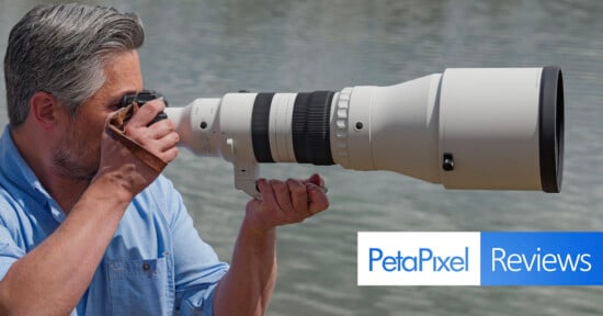 A man in a blue shirt takes a photo with a large telephoto camera lens near water. The image features the Petapixel Reviews logo in the bottom right corner.