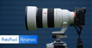 A large white Sony G Master telephoto camera lens mounted on a tripod, attached to a camera body, with a blue background and "PetaPixel Reviews" text overlay.