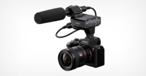 A Sony mirrorless camera equipped with a large lens, an external microphone, and an audio interface adapter mounted on top, all against a plain white background.