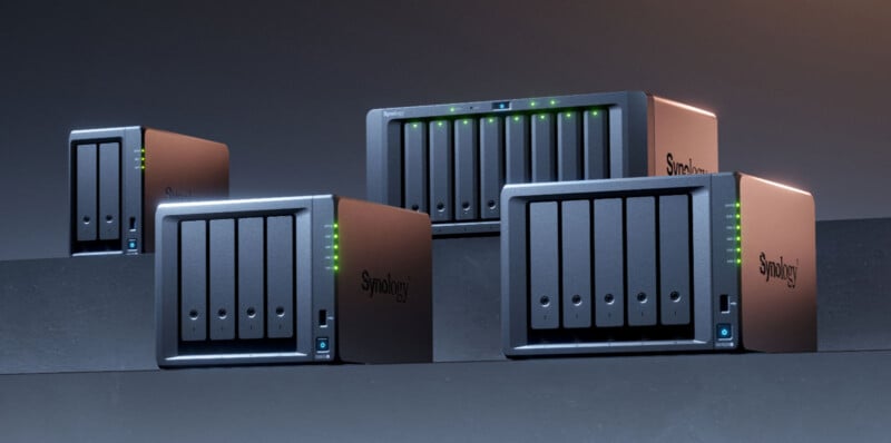 Four Synology network attached storage (NAS) devices are displayed on a dark surface, each with several drive bays and green LED indicator lights illuminated on the front panels.