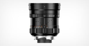 A black camera lens with manual focus and aperture rings, featuring white and orange markings for measurements, shown against a plain white background.