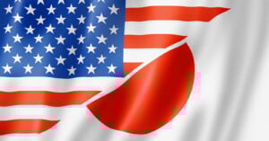 An image combining the United States and Japan flags, with the stars and stripes partially merging into the red circle from the Japanese flag on a white background, symbolizing a blend of both nations.